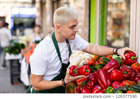 Guy shop seller puts bell pepper goods on display case Guy shop seller puts bell pepper goods on display case 126377590