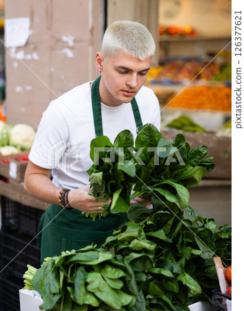 Grocery store employee places fresh spinach on display case at street store 126377621