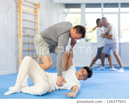 Concentrated man and guy in sport club during training, sparring and practicing technique of hand grab lying down 126377641