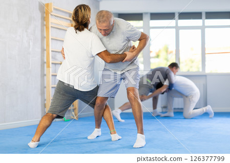 Man and senior man athletes in pair conduct training battle in oriental fighting technique Man and senior man athletes in pair conduct training battle in oriental fighting technique 126377799