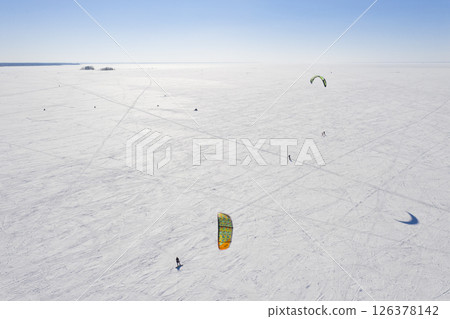 Aerial view of the snowy surface of a frozen lake and skiers with a parachute doing snowkiting 126378142
