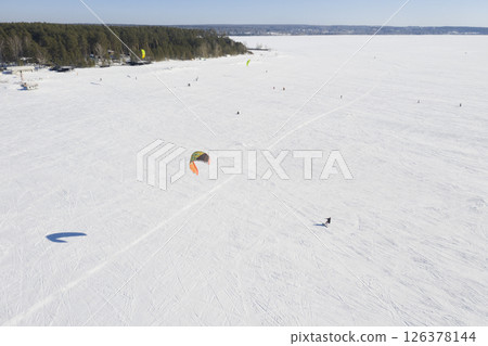 Aerial view of the snowy surface of a frozen lake and skiers with a parachute doing snowkiting 126378144