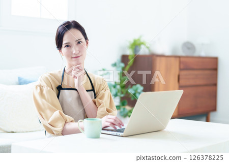 A housewife wearing an apron using a computer while thinking A housewife wearing an apron using a computer while thinking 126378225