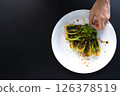 Hand adjusts a plate of bok choy garnished with seasoning, perfect for Asian cooking. 126378519