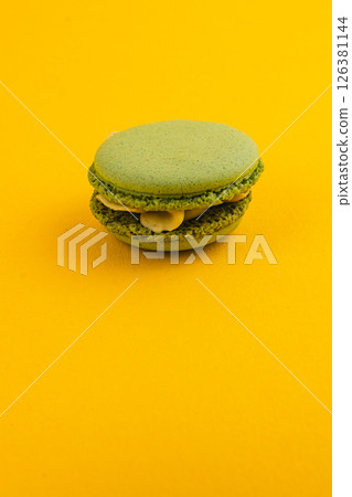 Green macaron on bright yellow background displays dessert art 126381144