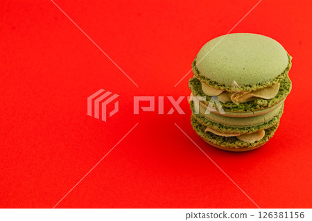 Delightful green macarons stacked on vibrant red backdrop Delightful green macarons stacked on vibrant red backdrop 126381156