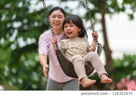 cheerful toddler girl with mother playing on a swing at playground 126381635