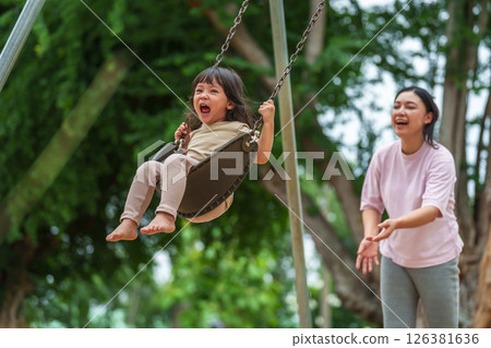 cheerful toddler girl with mother playing on a swing at playground 126381636