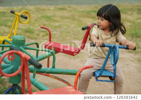 toddler girl having fun while playing on carousel at playground toddler girl having fun while playing on carousel at playground 126381642