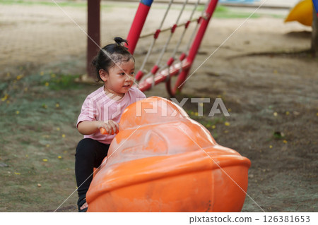 happy toddler girl riding jet ski toy at playground 126381653