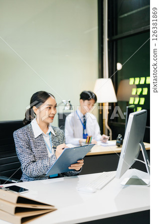 Asian female office worker business suits smiling at camera with working notepad, tablet and laptop documents 126381869
