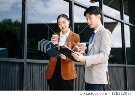 Businessman and woman going in city center in smart casual business style, talking, working together, stylish freelance people, holding coffee Businessman and woman going in city center in smart casual business style, talking, working together, stylish freelance people, holding coffee 126382055