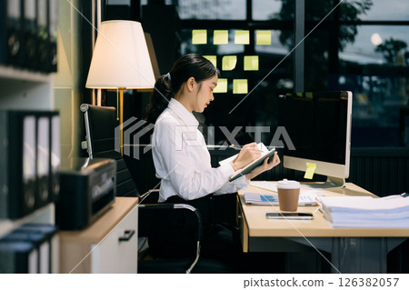Successful Asian Businesswoman Analyzing Finance on Tablet and Laptop at modern Office Desk tax, report, 126382057