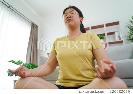Asian woman meditate and practice yoga in the living room at home, home health care, exercise. Asian woman meditate and practice yoga in the living room at home, home health care, exercise. 126382059