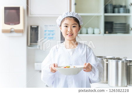 A girl on school lunch duty wearing a white coat and holding a plate 126382228