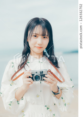 Girl holding a film camera on the beach 126382702