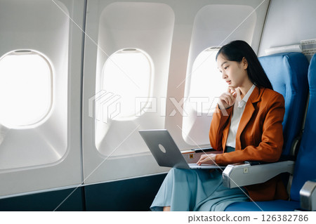Asian executive excels in first class, multitasking with digital tablet, laptop. Travel in style, work with grace. Asian executive excels in first class, multitasking with digital tablet, laptop. Travel in style, work with grace. 126382786