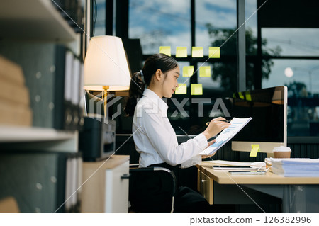 Successful Asian Businesswoman Analyzing Finance on Tablet and Laptop at modern Office Desk tax, report, 126382996