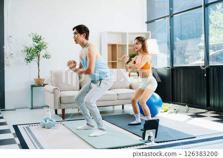 Fitness duo high fiving during an energetic workout session at home, featuring yoga mats, gym equipment 126383200
