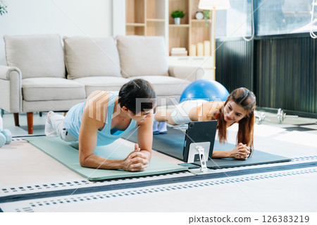 Fitness duo high fiving during an energetic workout session at home, featuring yoga mats, gym equipment 126383219