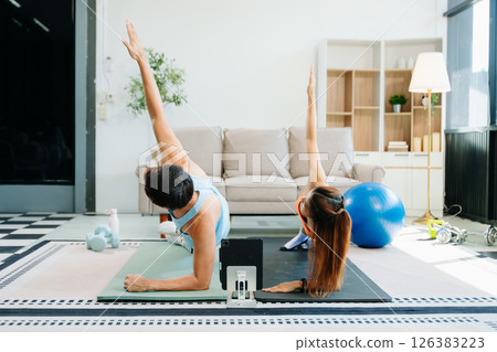 Fitness duo high fiving during an energetic workout session at home, featuring yoga mats, gym equipment Fitness duo high fiving during an energetic workout session at home, featuring yoga mats, gym equipment 126383223