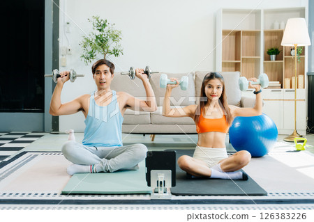 Fitness duo high fiving during an energetic workout session at home, featuring yoga mats, gym equipment 126383226