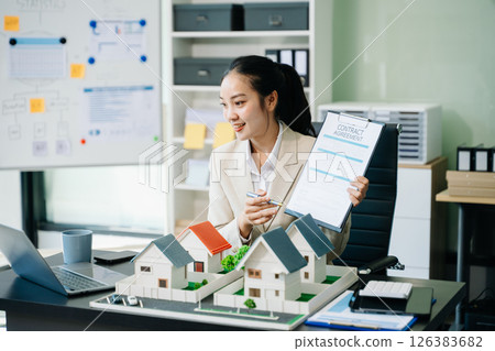 Young real estate agent worker working with laptop and tablet at table and small house beside it. Young real estate agent worker working with laptop and tablet at table and small house beside it. 126383682