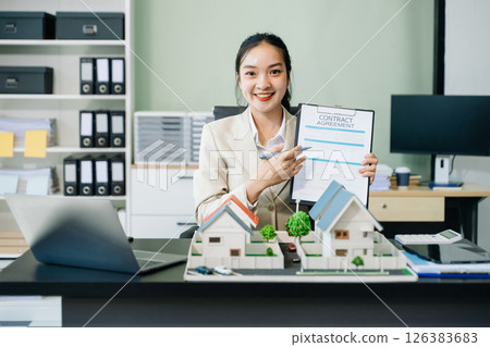 Young real estate agent worker working with laptop and tablet at table and small house beside it. 126383683