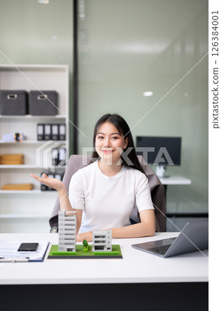 Young real estate agent worker working with laptop and tablet at table in office and small house beside it. 126384001