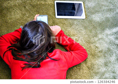 Girl in a red sweater lying in the meadow with a white tablet Girl in a red sweater lying in the meadow with a white tablet 126384246
