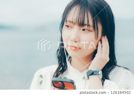 A young woman operating a smartphone with a calm sea in the background 126384502