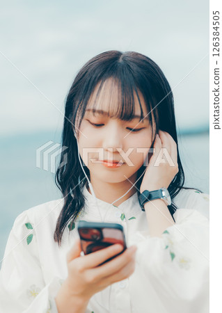 一位年輕女子在平靜的海面背景下操作智慧型手機 一位年輕女子在平靜的海面背景下操作智慧型手機 126384505
