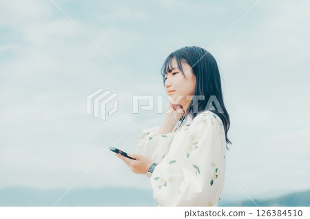 A young woman operating a smartphone with a calm sea in the background 126384510
