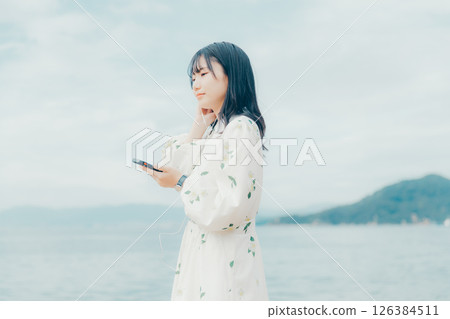 A young woman operating a smartphone with a calm sea in the background A young woman operating a smartphone with a calm sea in the background 126384511