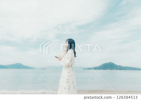 A young woman operating a smartphone with a calm sea in the background 126384513