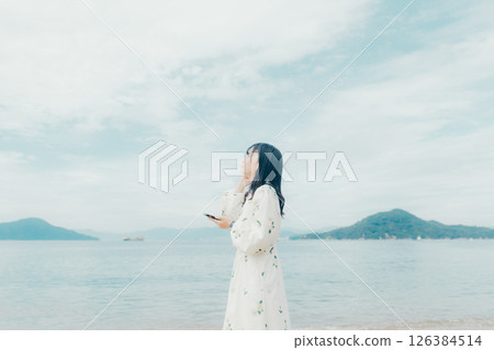 一位年輕女子在平靜的海面背景下操作智慧型手機 一位年輕女子在平靜的海面背景下操作智慧型手機 126384514
