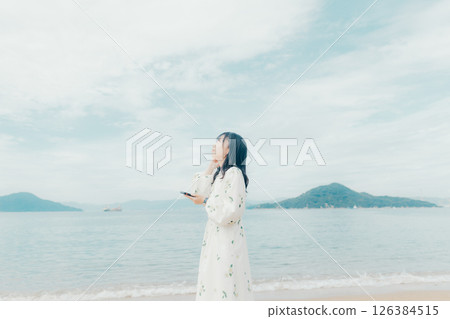 一位年輕女子在平靜的海面背景下操作智慧型手機 一位年輕女子在平靜的海面背景下操作智慧型手機 126384515