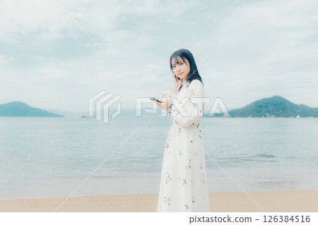 一位年輕女子在平靜的海面背景下操作智慧型手機 一位年輕女子在平靜的海面背景下操作智慧型手機 126384516