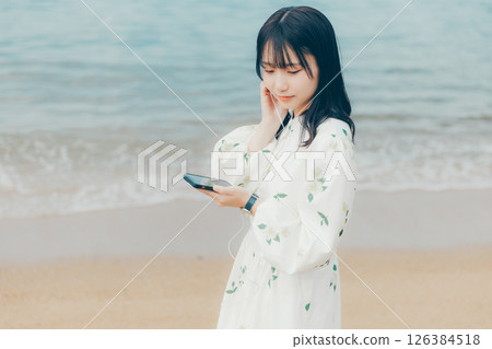 A young woman operating a smartphone with a calm sea in the background A young woman operating a smartphone with a calm sea in the background 126384518
