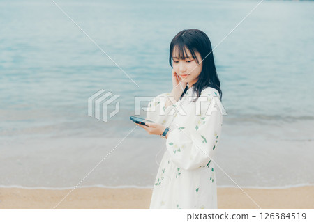A young woman operating a smartphone with a calm sea in the background A young woman operating a smartphone with a calm sea in the background 126384519