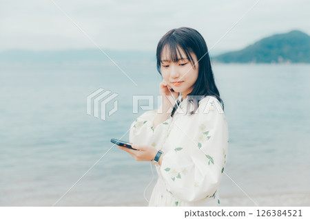 一位年輕女子在平靜的海面背景下操作智慧型手機 126384521