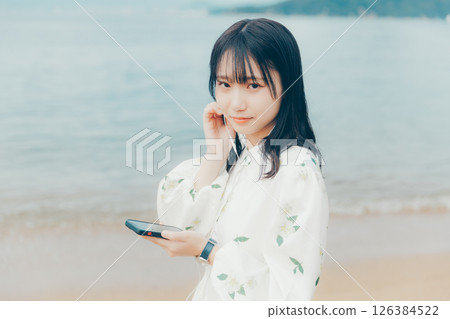 一位年輕女子在平靜的海面背景下操作智慧型手機 一位年輕女子在平靜的海面背景下操作智慧型手機 126384522