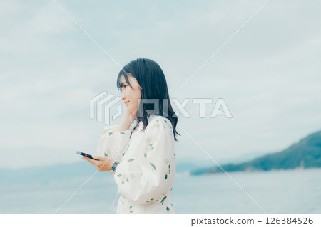 A young woman operating a smartphone with a calm sea in the background 126384526