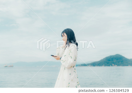 A young woman operating a smartphone with a calm sea in the background 126384529