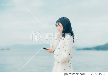 A young woman operating a smartphone with a calm sea in the background 126384532