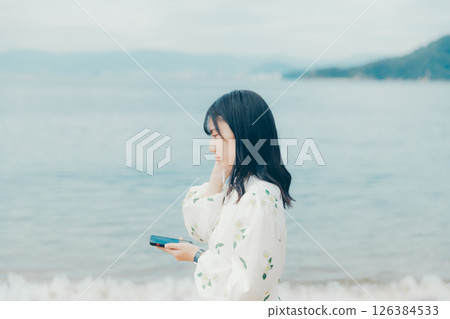 A young woman operating a smartphone with a calm sea in the background 126384533