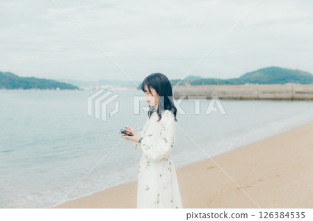 A young woman operating a smartphone with a calm sea in the background 126384535