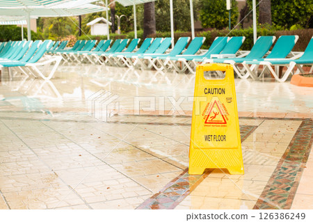 Warning sign caution wet floor among pool deck chairs near the hotel swimming pool 126386249