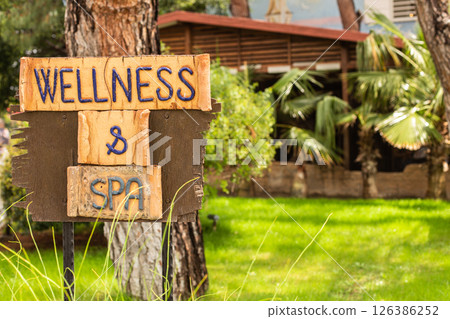 Wooden sign with inscription wellness and spa on green garden background. Wooden sign with inscription wellness and spa on green garden background. 126386252