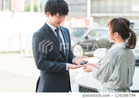 年輕銷售員將車鑰匙交給女顧客，男銷售員 126386794